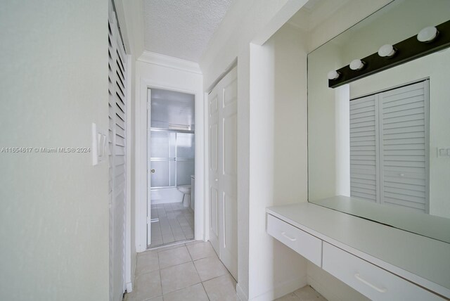 hallway with light tile patterned floors, crown molding, and a textured ceiling