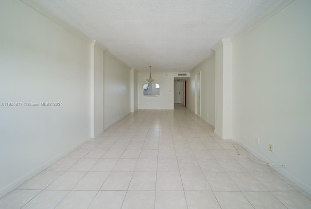 empty room with light tile patterned floors, ornamental molding, and a textured ceiling