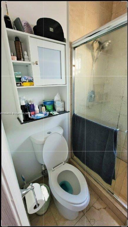 bathroom with tile patterned flooring, toilet, and a shower with door