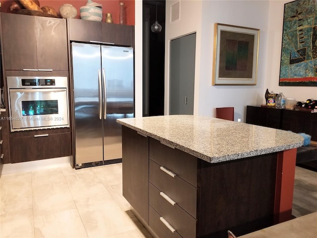 kitchen with a center island, light stone counters, stainless steel appliances, and dark brown cabinetry