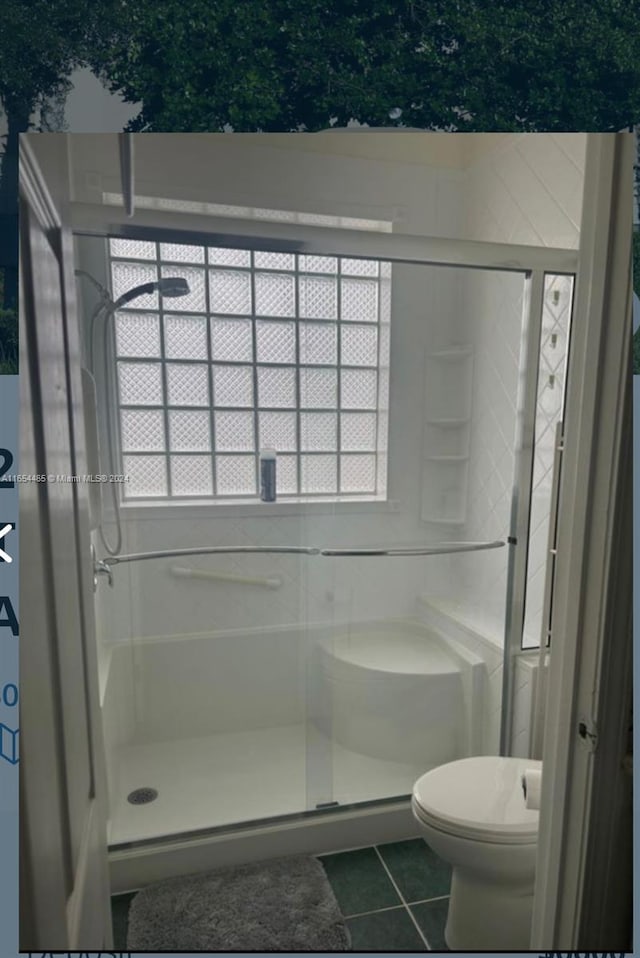 bathroom featuring a shower with shower door, toilet, and tile patterned flooring