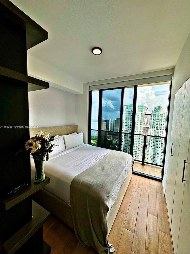 bedroom featuring multiple windows, floor to ceiling windows, access to exterior, and light hardwood / wood-style flooring