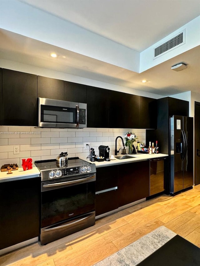 kitchen featuring tasteful backsplash, sink, light wood-type flooring, and black appliances