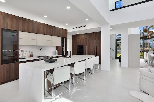 kitchen with a kitchen bar, tasteful backsplash, sink, white cabinets, and an island with sink