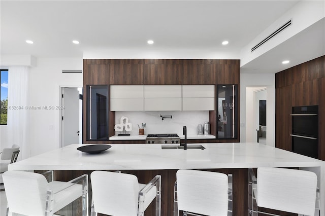 kitchen with a kitchen bar, a center island with sink, white cabinetry, and sink