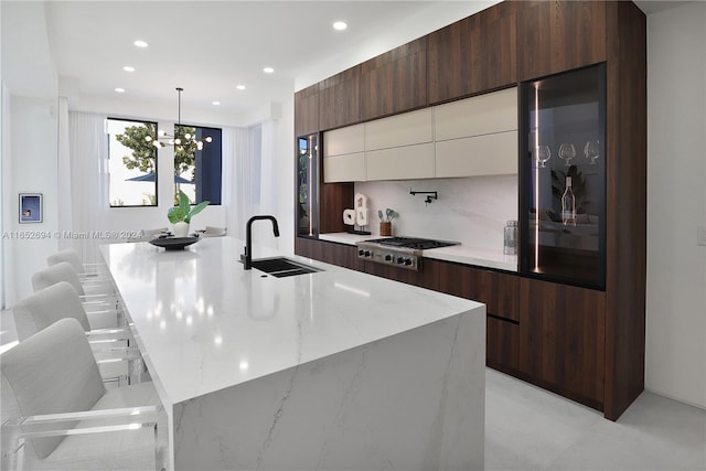 kitchen featuring a kitchen island with sink, sink, white cabinets, and decorative light fixtures