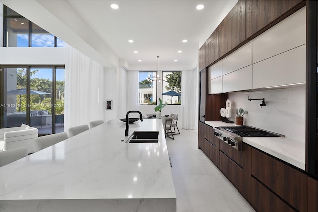 kitchen featuring light stone countertops, sink, a large island with sink, white cabinetry, and hanging light fixtures