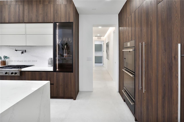 kitchen with dark brown cabinetry, light stone countertops, tasteful backsplash, white cabinetry, and stainless steel gas cooktop