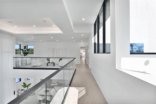 hall with a healthy amount of sunlight, light wood-type flooring, and a tray ceiling