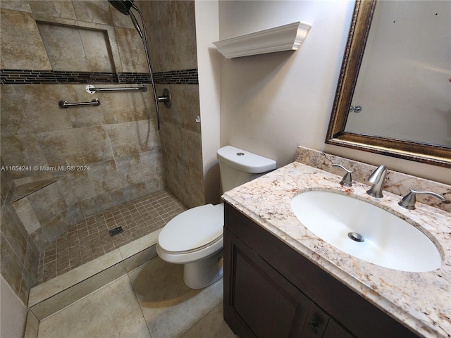 bathroom with toilet, tile patterned floors, tiled shower, and vanity