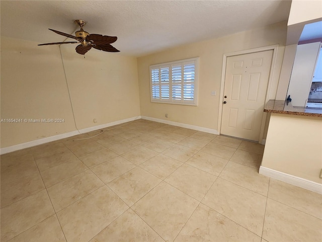spare room featuring light tile patterned floors, baseboards, a ceiling fan, and a textured ceiling