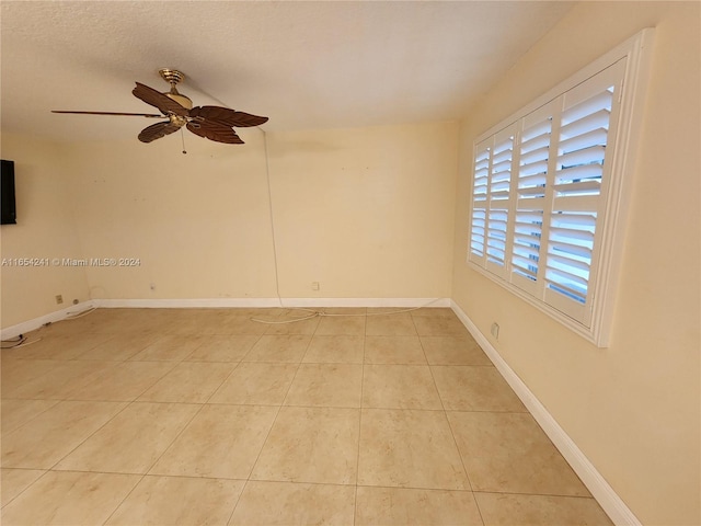 empty room featuring a textured ceiling, light tile patterned floors, ceiling fan, and baseboards