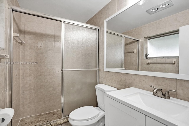 bathroom with tile walls, toilet, a shower with door, and vanity