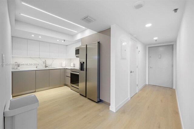 kitchen featuring appliances with stainless steel finishes, backsplash, sink, and light hardwood / wood-style flooring