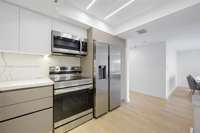 kitchen featuring light wood-type flooring, tasteful backsplash, light stone counters, and stainless steel appliances