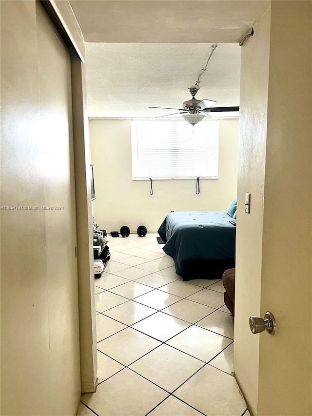 bedroom featuring ceiling fan, light tile patterned floors, and a textured ceiling