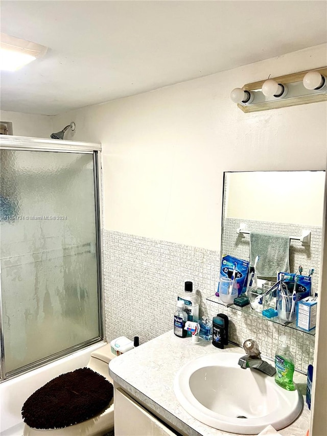 full bathroom featuring vanity, backsplash, combined bath / shower with glass door, tile walls, and toilet