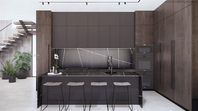 kitchen featuring a kitchen breakfast bar, backsplash, oven, dark brown cabinetry, and sink