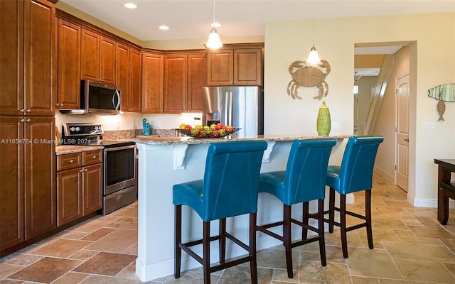 kitchen featuring pendant lighting, a kitchen breakfast bar, light stone counters, a kitchen island, and appliances with stainless steel finishes