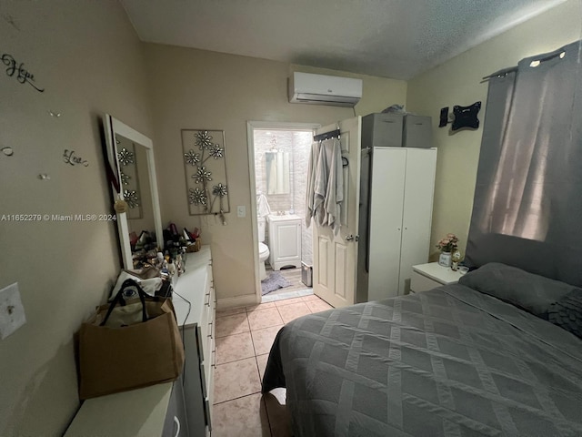 bedroom with a wall mounted AC, ensuite bath, a textured ceiling, and light tile patterned flooring