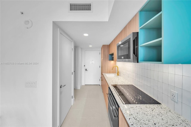 kitchen with backsplash, light stone countertops, sink, and black appliances