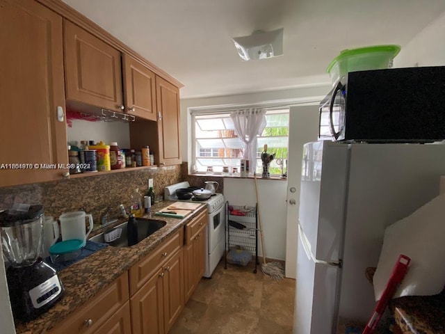 kitchen featuring dark stone countertops, backsplash, white appliances, sink, and light tile patterned flooring