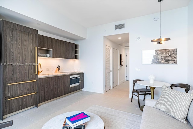 kitchen featuring tasteful backsplash, oven, dark brown cabinetry, decorative light fixtures, and light tile patterned floors