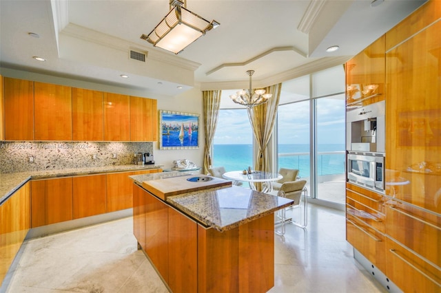 kitchen with a notable chandelier, stone counters, ornamental molding, tasteful backsplash, and a center island