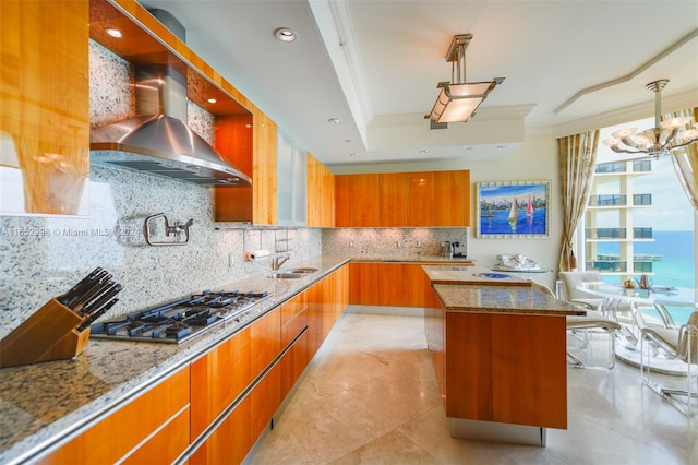 kitchen featuring decorative light fixtures, wall chimney exhaust hood, light stone countertops, tasteful backsplash, and a center island