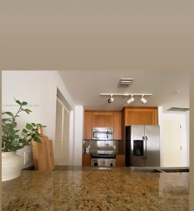 kitchen featuring stone counters, stainless steel appliances, rail lighting, and tasteful backsplash