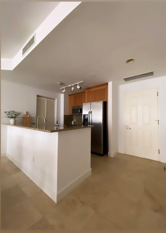 kitchen with kitchen peninsula, backsplash, dark stone countertops, sink, and stainless steel appliances