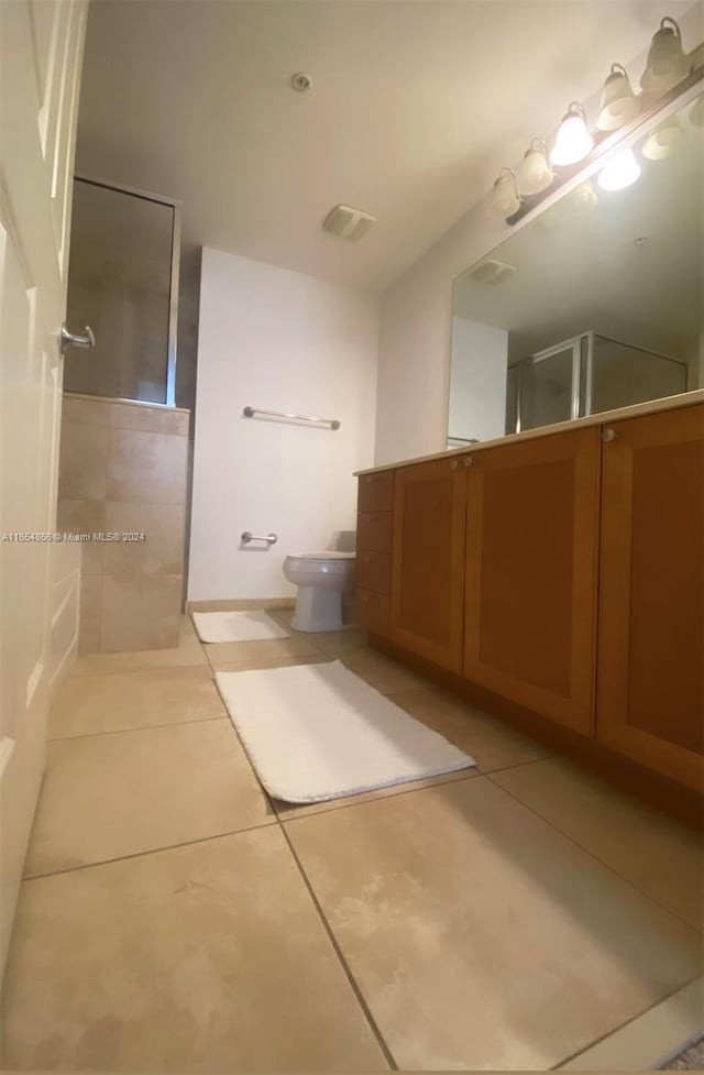 bathroom with toilet, vanity, tile patterned floors, and tiled shower