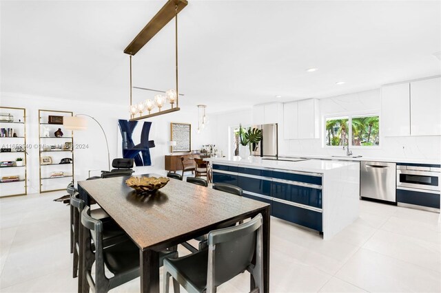 kitchen featuring dishwasher, a kitchen island, light tile patterned flooring, decorative light fixtures, and white cabinets