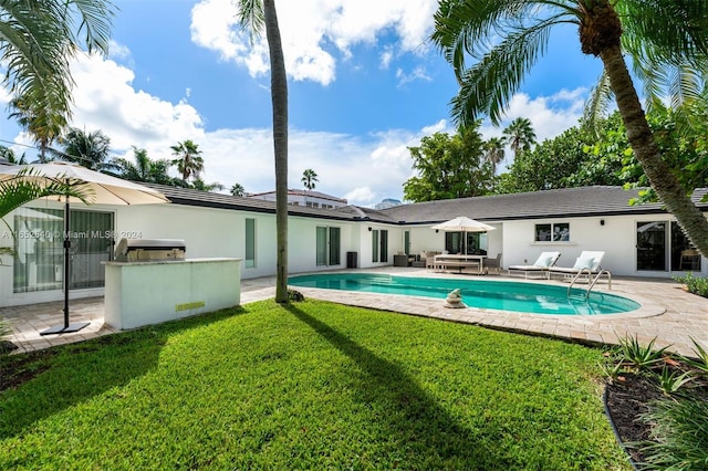 view of pool with a lawn, a patio, an outdoor hangout area, and exterior kitchen