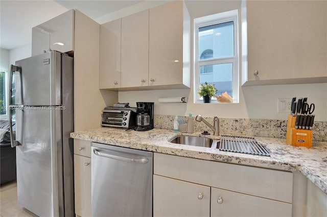 kitchen with stainless steel appliances, sink, light stone counters, and cream cabinetry