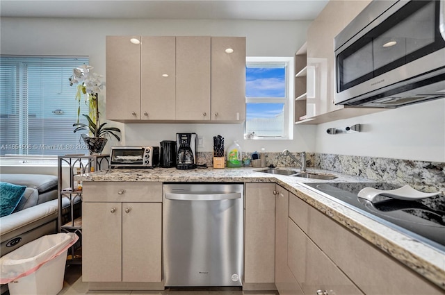 kitchen featuring sink, light stone countertops, cream cabinetry, and appliances with stainless steel finishes