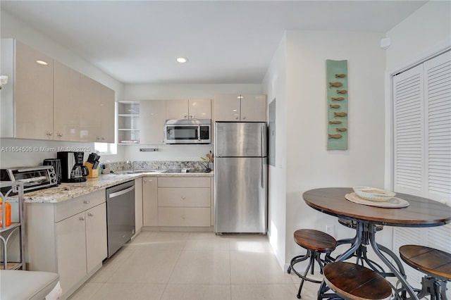 kitchen with light stone counters, light tile patterned flooring, cream cabinetry, and appliances with stainless steel finishes