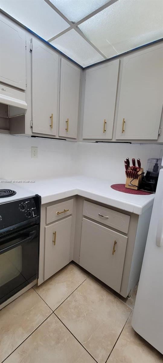 kitchen with gray cabinets, black range, and light tile patterned floors