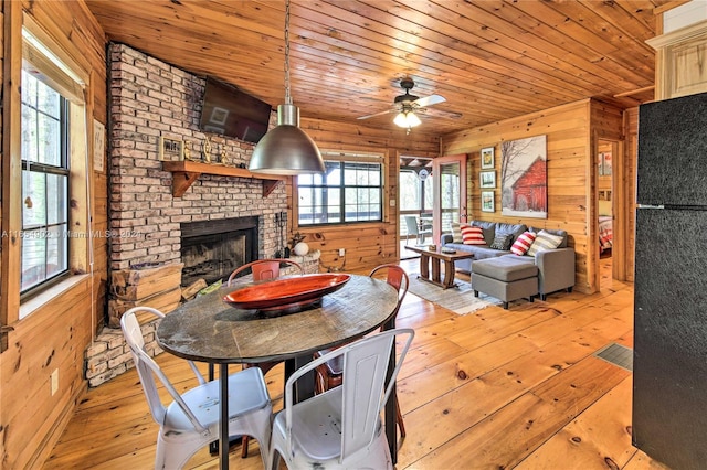 dining room featuring a brick fireplace, wood walls, wooden ceiling, ceiling fan, and light hardwood / wood-style flooring