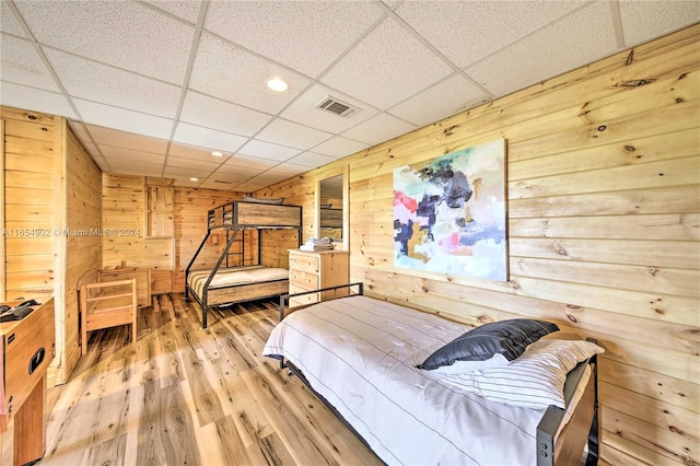 bedroom with a drop ceiling, wood walls, and hardwood / wood-style flooring