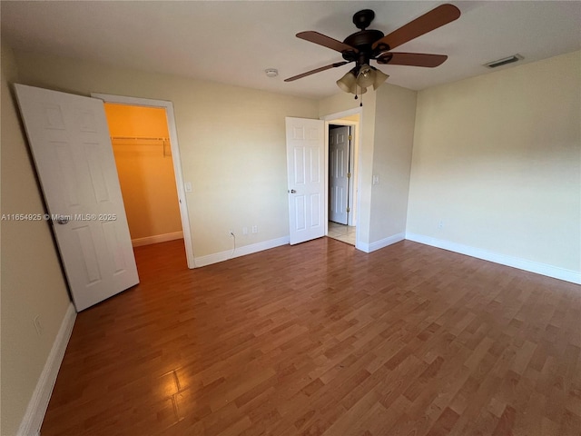 unfurnished bedroom featuring a walk in closet, ceiling fan, a closet, and dark hardwood / wood-style flooring