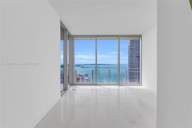 spare room featuring a water view, plenty of natural light, and a wall of windows