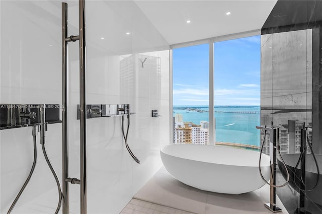 bathroom with floor to ceiling windows, a washtub, tile patterned flooring, a water view, and tile walls