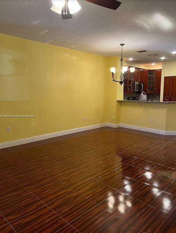 unfurnished living room with ceiling fan with notable chandelier, dark hardwood / wood-style flooring, and a textured ceiling