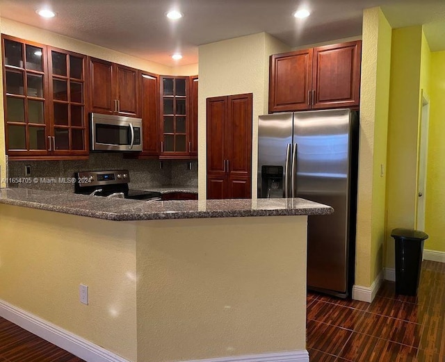 kitchen featuring appliances with stainless steel finishes, dark hardwood / wood-style floors, dark stone counters, kitchen peninsula, and decorative backsplash