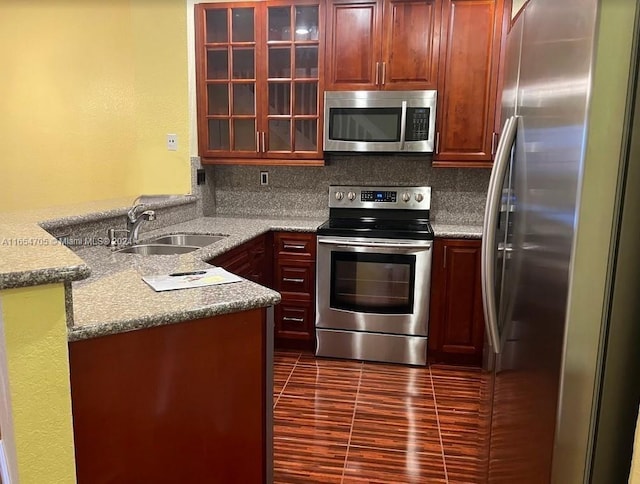 kitchen with appliances with stainless steel finishes, light stone counters, sink, kitchen peninsula, and decorative backsplash