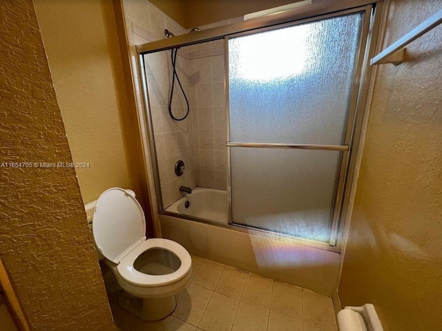 bathroom featuring a textured wall, shower / bath combination with glass door, tile patterned floors, and toilet