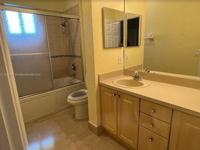 full bath featuring a textured wall, tile patterned floors, toilet, bath / shower combo with glass door, and vanity