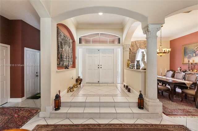 tiled entryway with ornate columns, ornamental molding, and a notable chandelier