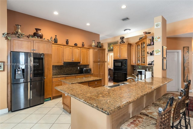 kitchen with tasteful backsplash, kitchen peninsula, stone countertops, black appliances, and a kitchen bar